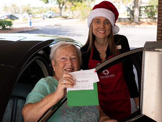 Two women in a SACFCU Drive through, with one woman holding up a gift card she won from the credit union.