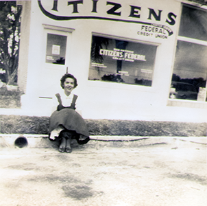 One of our early members sits in front of our very first branch location in the 1947 Herrmann Building