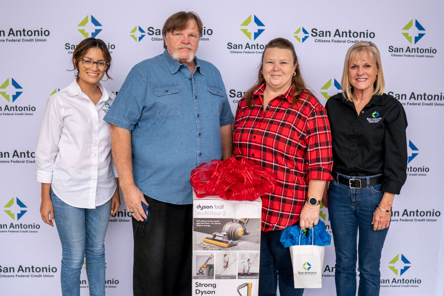 Two SACFCU employees giving a prize of a Dyson Vacuum to the winner of our Bill Pay contest.