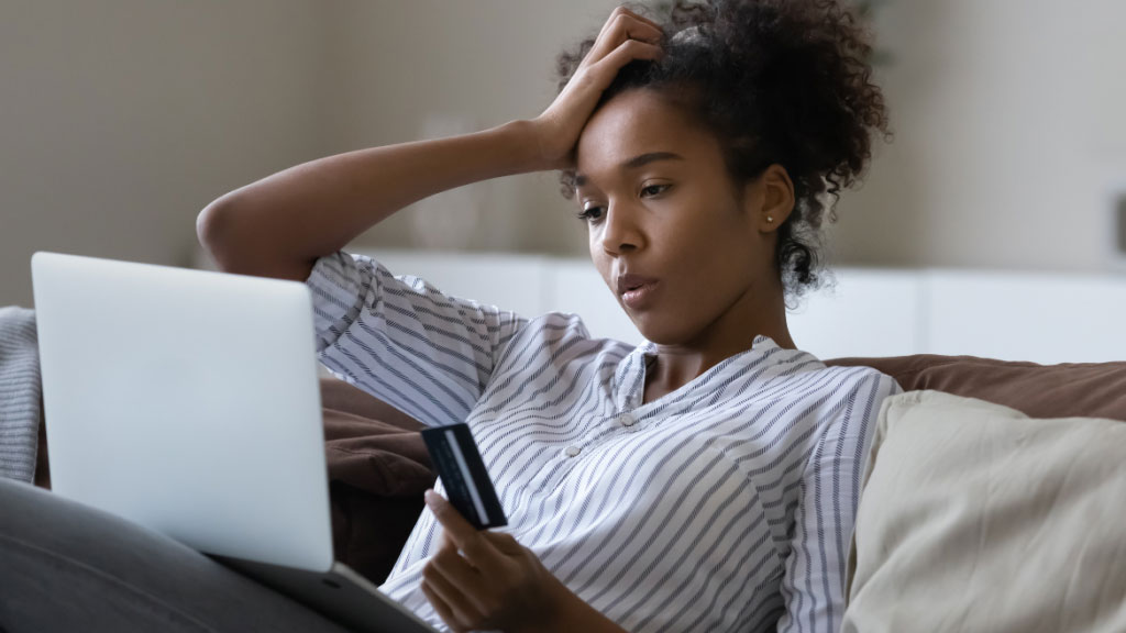 Woman holding her head in frustration while making card payment on a laptop